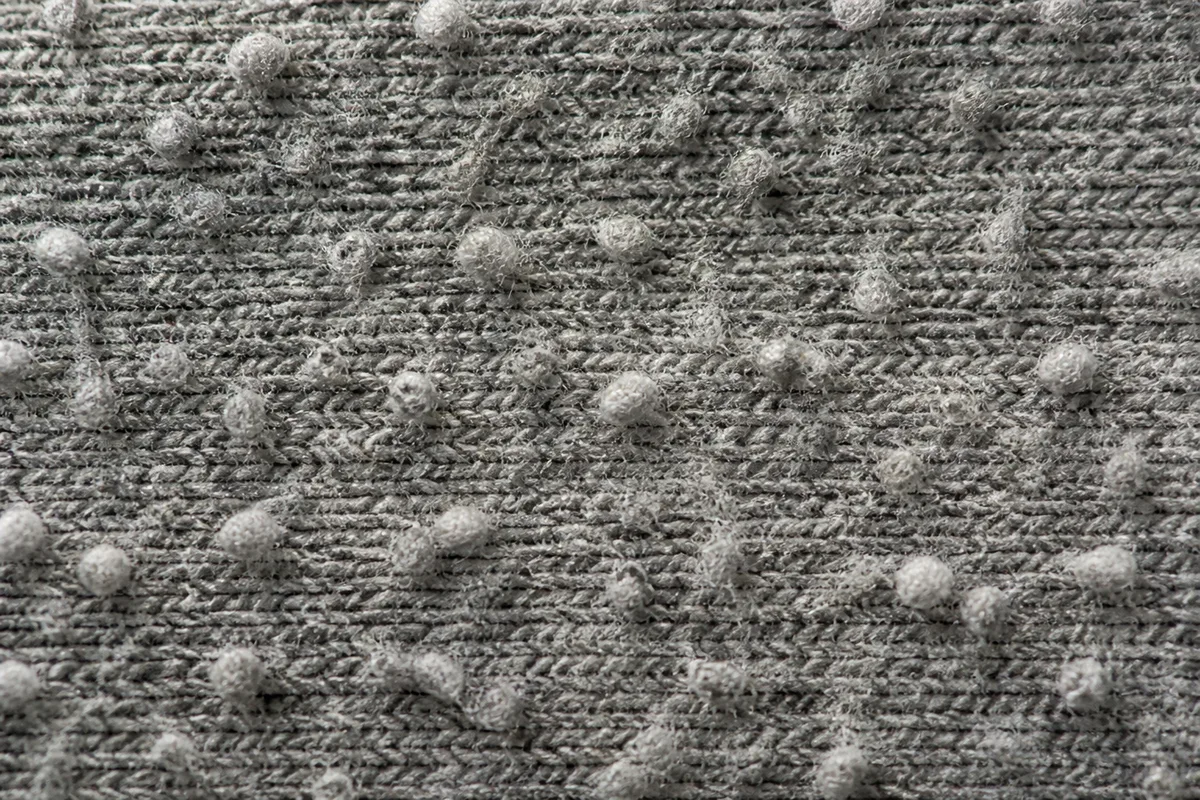 Détail d’une maille de pull en laine grise couverte de petites bouloches en lumière rasante